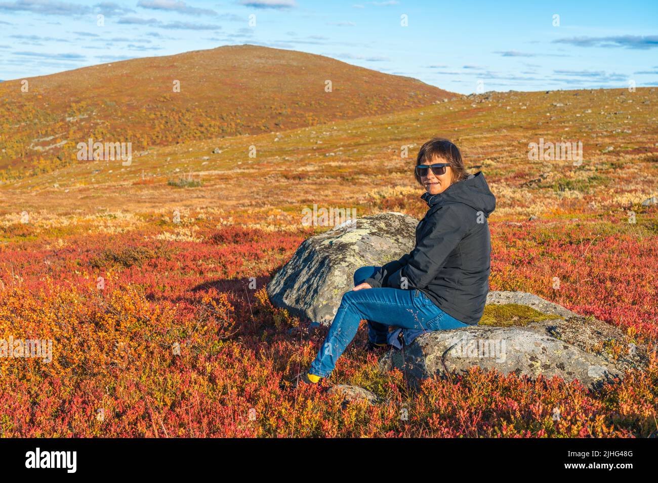 Woman sitting on a rock on Mount Dundret in autumn season with nice colors, Gällivare, Swedish Lapland, Sweden Stock Photo