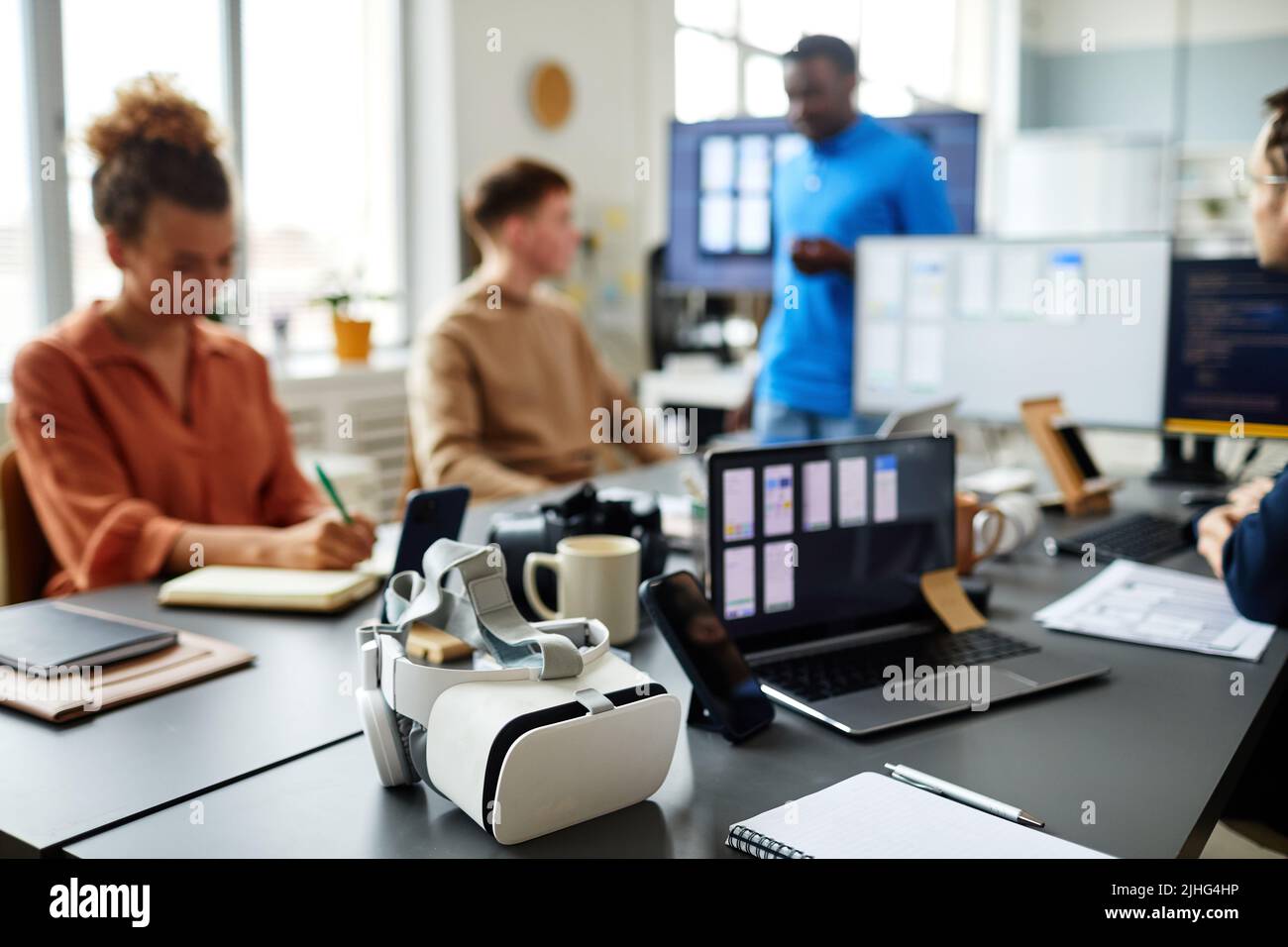 Horizontal image of VR glasses lying on table while programmers testing new software in background Stock Photo