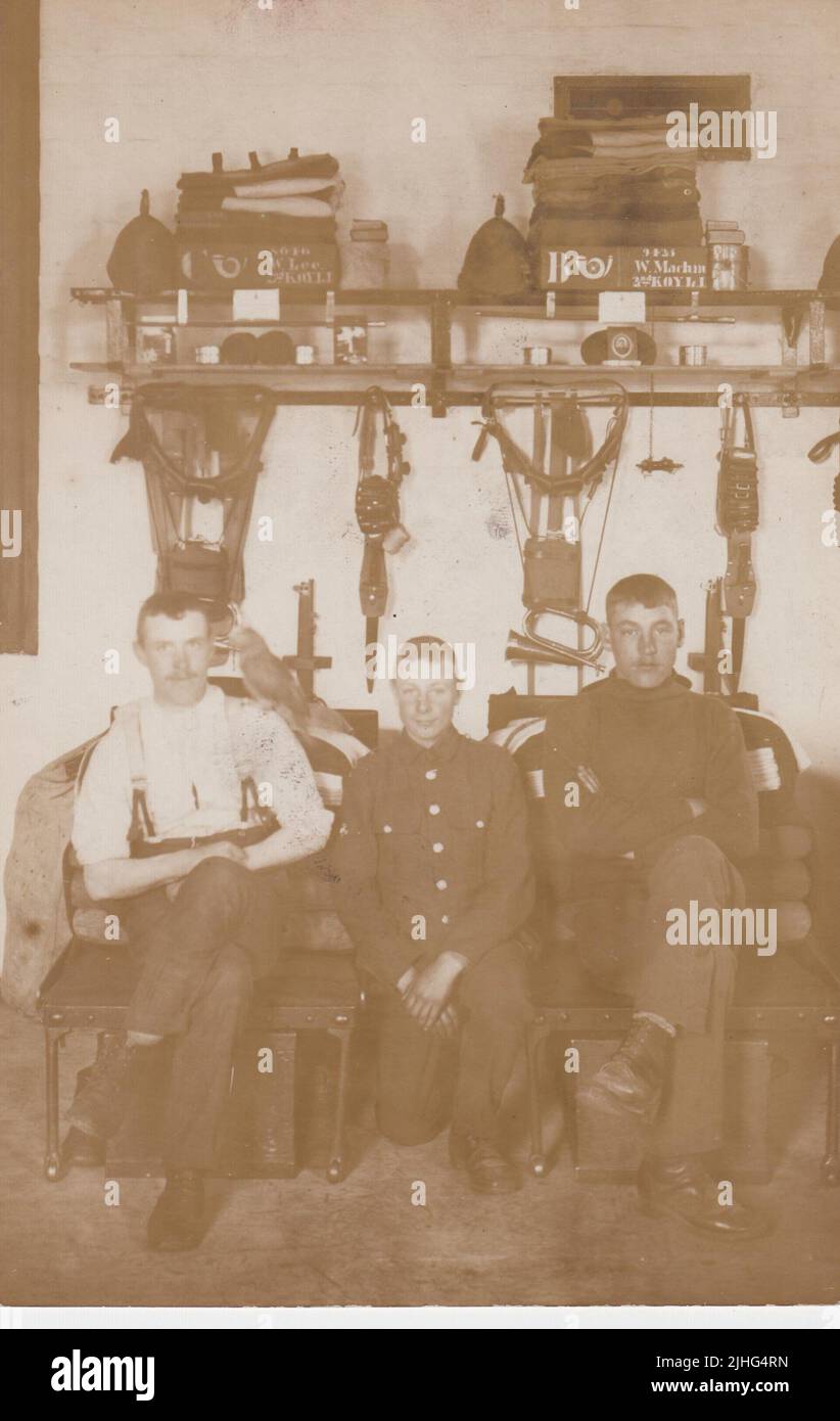 Three musicians or bandsmen in the King's Own Yorkshire Light Infantry (KOYLI) photographed in the barracks bed spaces of W. Lee and W. Machin, early 20th century. The kit of the soldiers is neatly arranged on shelves behind them, including helmets, bedding, mess tins, books, weaponry and bugles. One soldier has a parrot on his shoulder Stock Photo