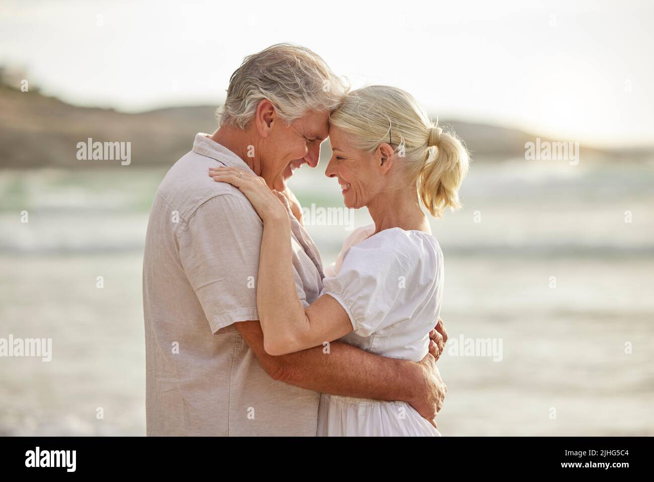 Closeup of a happy senior caucasian couple standing and embracing each other on a day out at the beach. Mature husband and wife smiling and showing Stock Photo