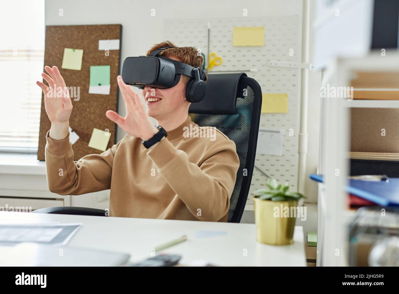 Young programmer sitting at table at office and gesturing, he testing virtual reality glasses Stock Photo