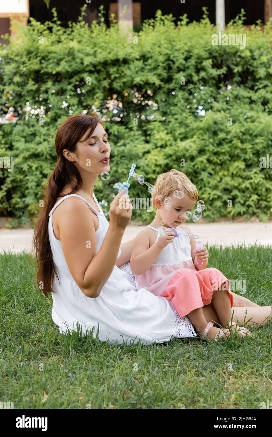 Mother and child blowing soap bubbles on meadow in park Stock Photo