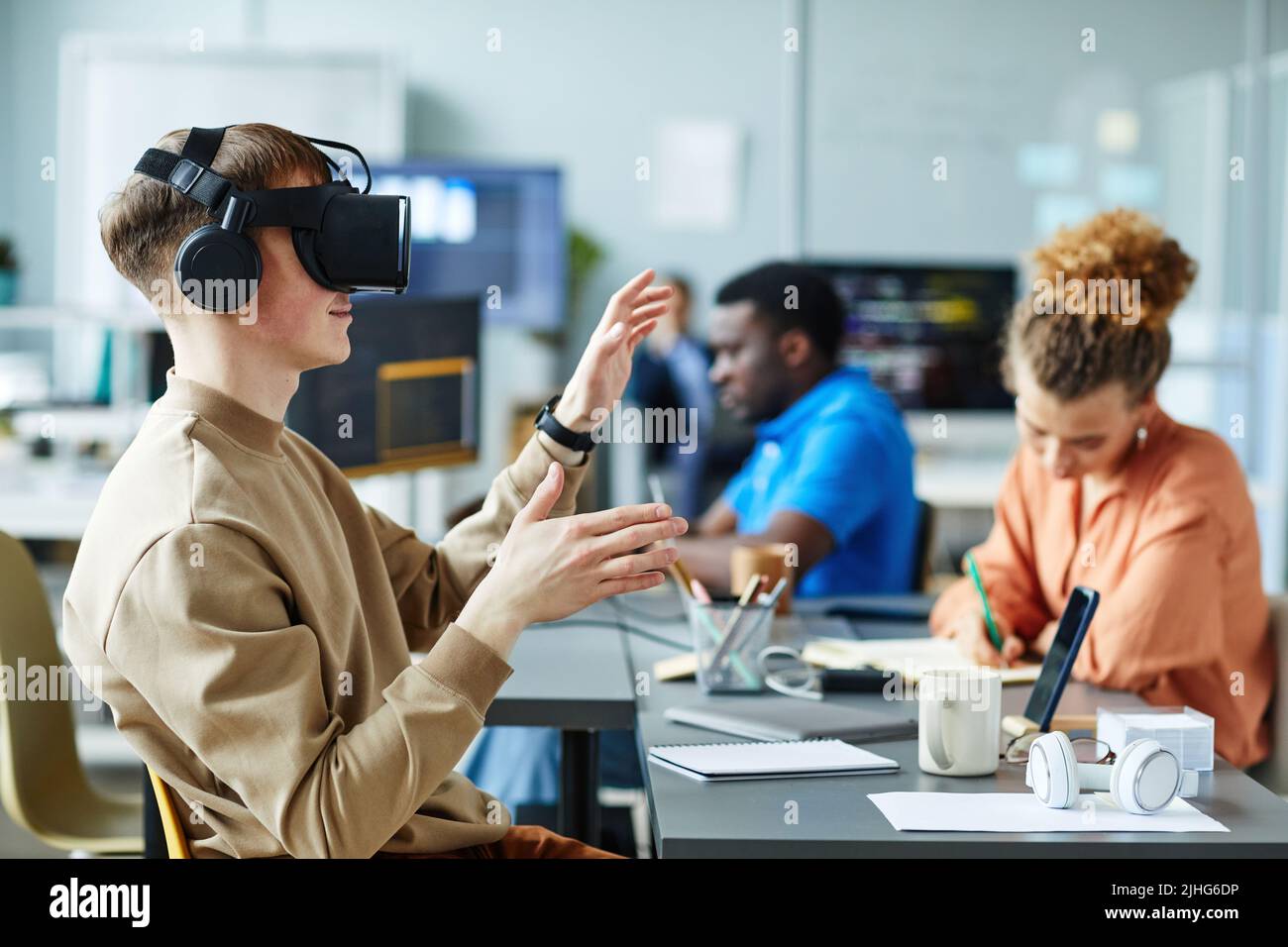 Young man in virtual reality glasses sitting at meeting with colleagues and testing new VR application Stock Photo