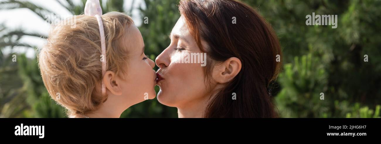 Side view of brunette mother kissing baby daughter outdoors in Valencia, banner Stock Photo
