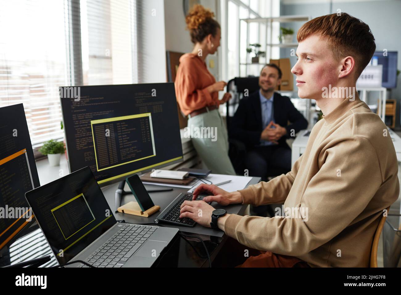 Young programmer typing on keyboard and looking at computer monitor working at table, he writing codes for new software Stock Photo