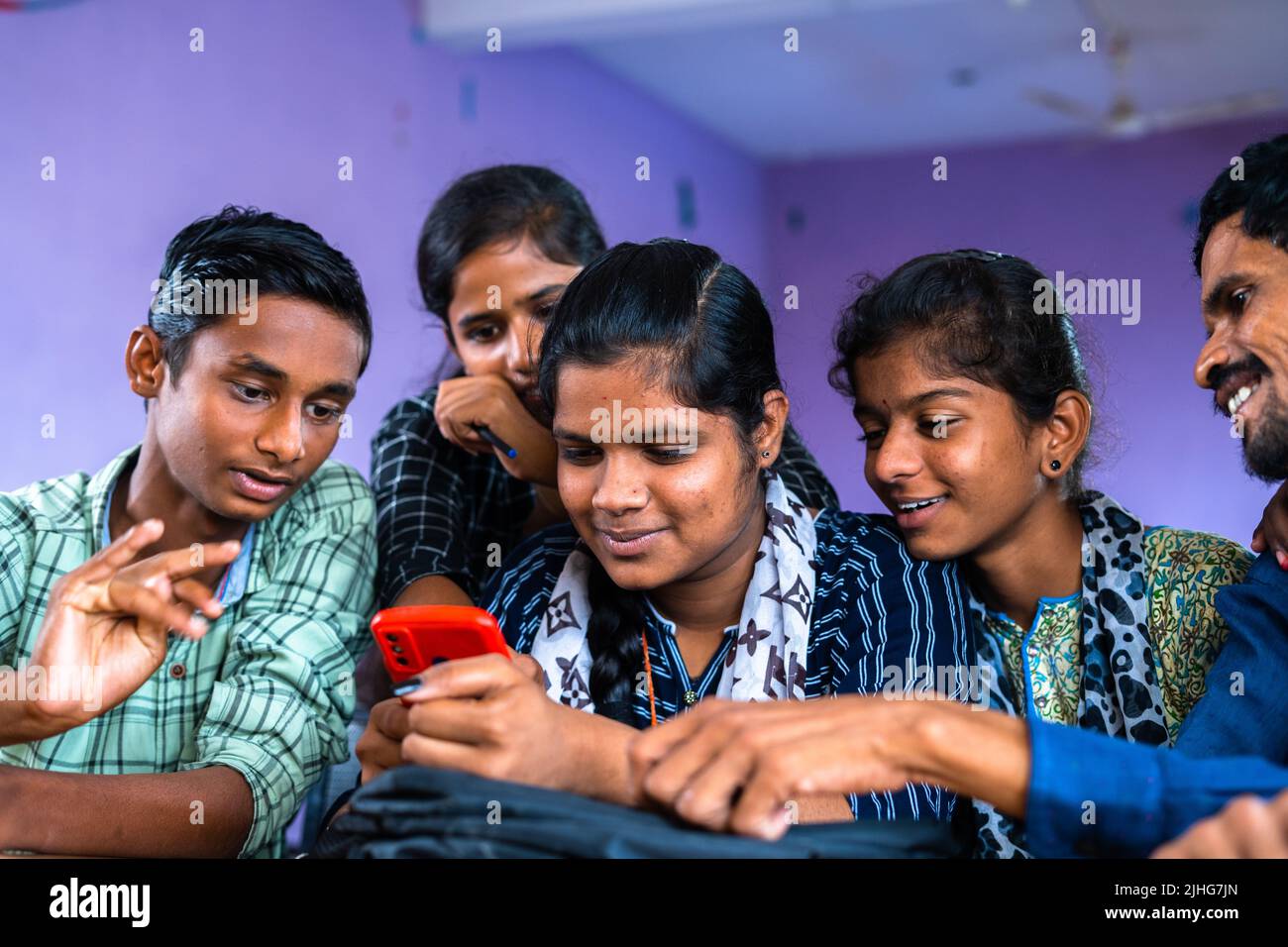 Group of excited college students checking exam results on mobile phone at classroom - concept of education, friendship and happiness Stock Photo