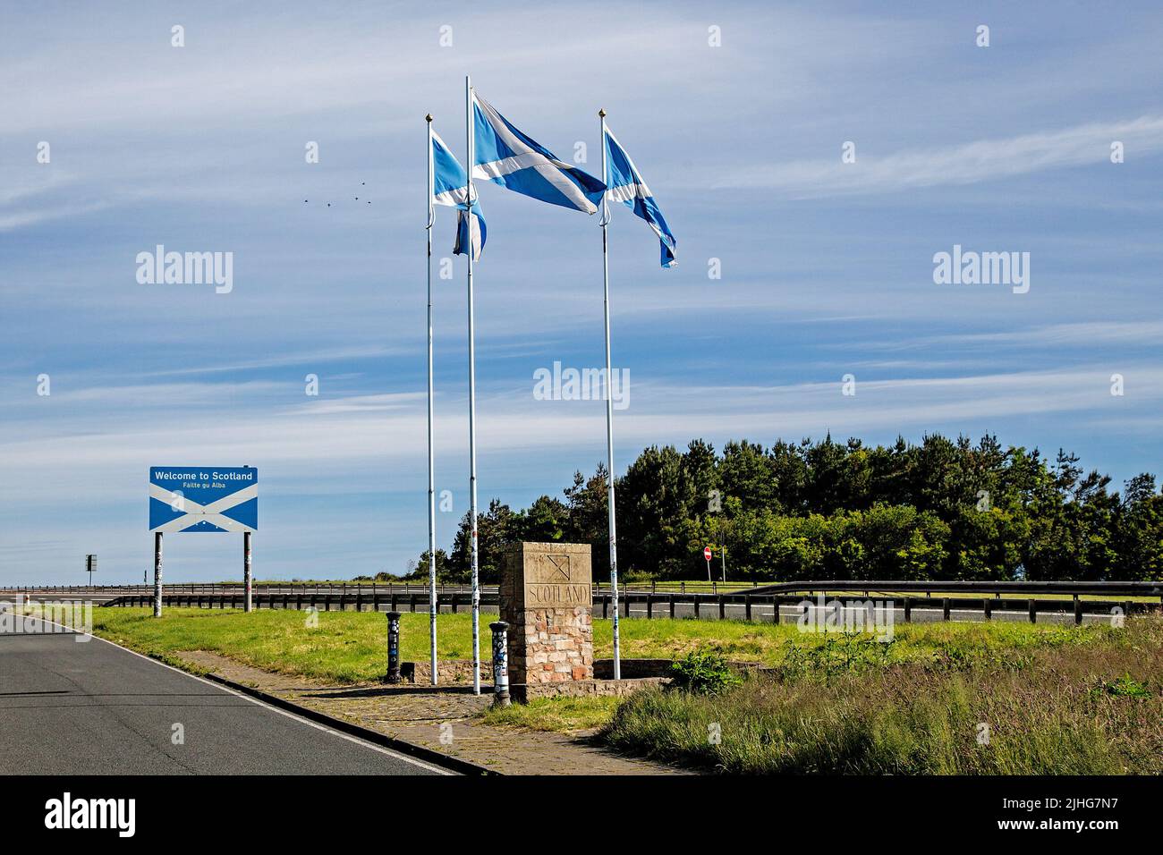 The border between England and Scotland at Berwick-Upon-Tweed is marked by the Scottish flags and a stone plinth. A bright blue sky with wispy clouds. Stock Photo