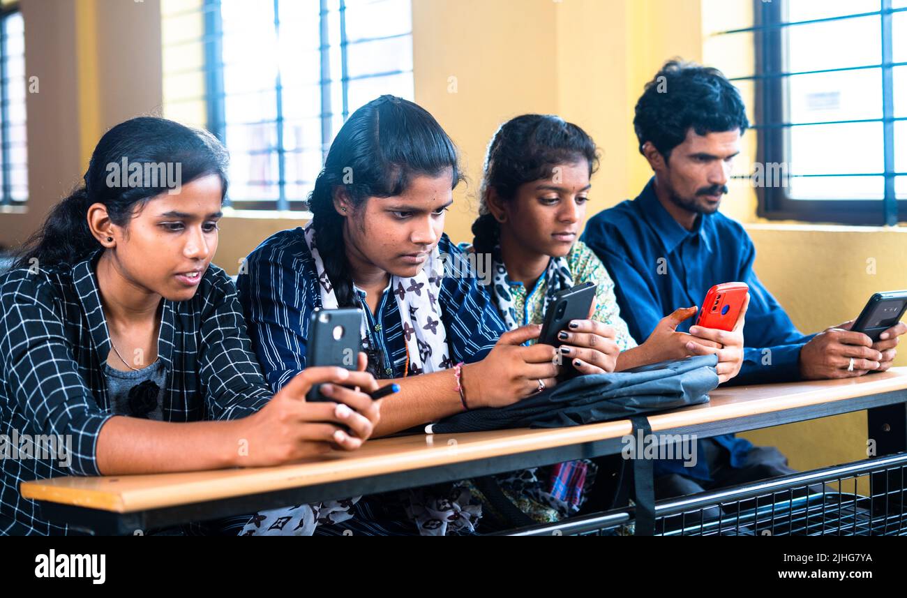 Group of teenager students busy using mobile phone while sitting on classroom - concept of technology, social media addiction and friendship. Stock Photo