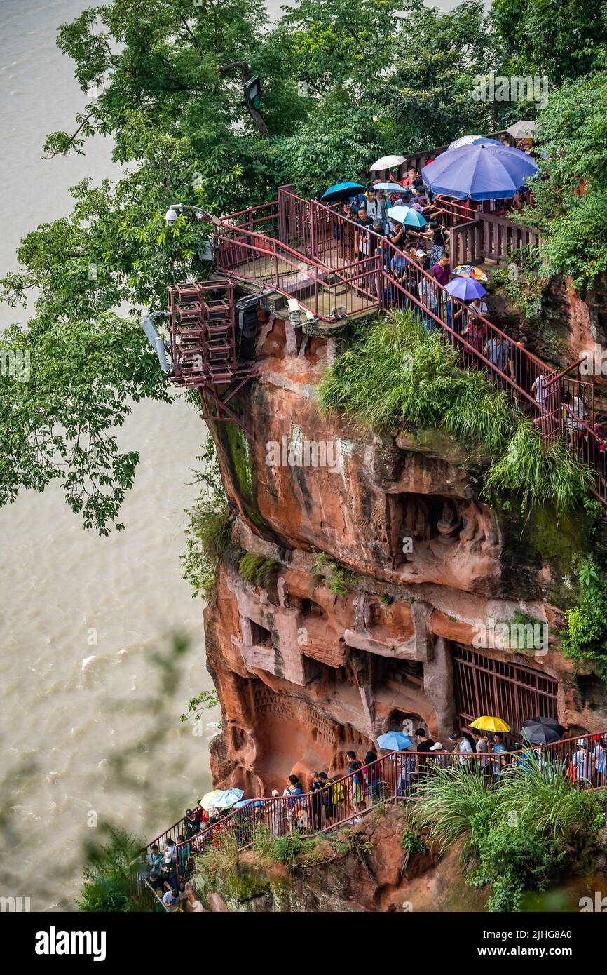 Leshan, China - July 2019 : Crowds of tourists walking down the plank walk around Giant  Leshan Buddha monument, a 71-meter tall stone statue built be Stock Photo