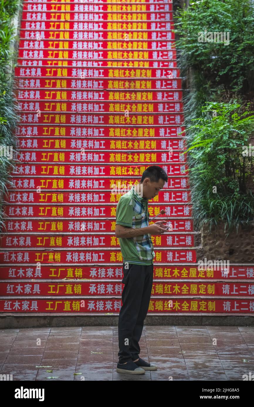 Zigong, China - July 2019 : Street scene in the city of Zigong in summer, man  looking at the screen of his mobile phone reading and texting Stock Photo