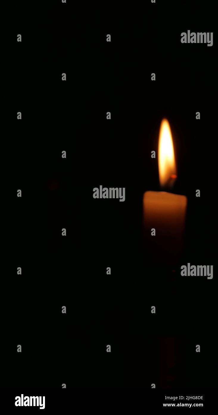 Vertical image of glowing candle and flame against black background ...