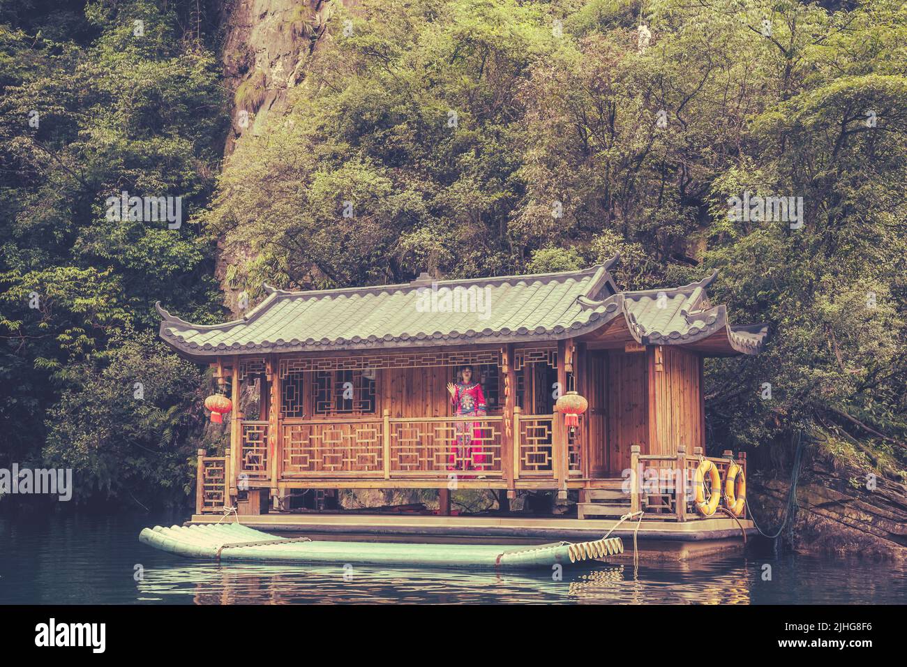 Zhangjiajie, China -  August 2019 : Chinese woman dressed in traditional ethnic minority costume standing on the porch of an old wooden floating house Stock Photo