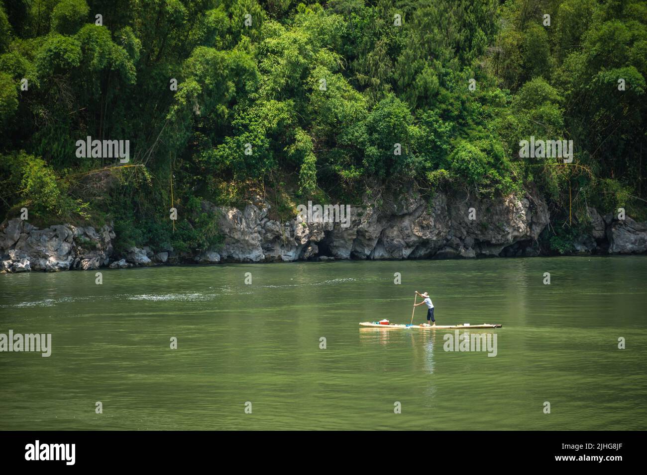Yangshuo, China - August 2019 : Old fisherman paddling on a small narrow wooden boat among stunning karst mountain scenery on the magnificent Li river Stock Photo