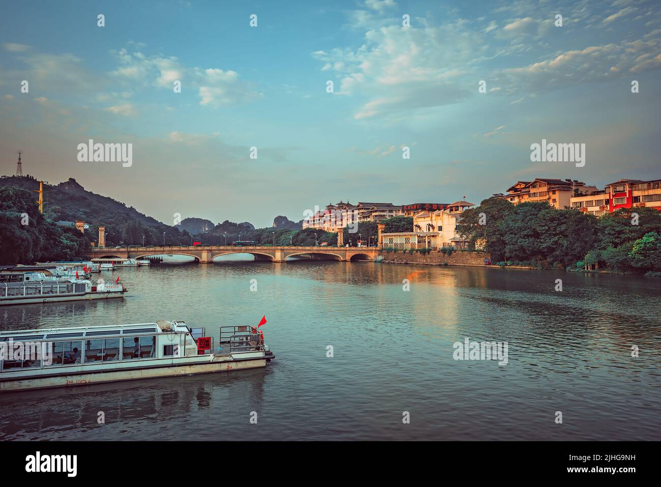 Guilin, China - August 2019 : Barges docked on the riverside with arched road bridge over magnificent Li River in the background, Guilin town, Guangxi Stock Photo