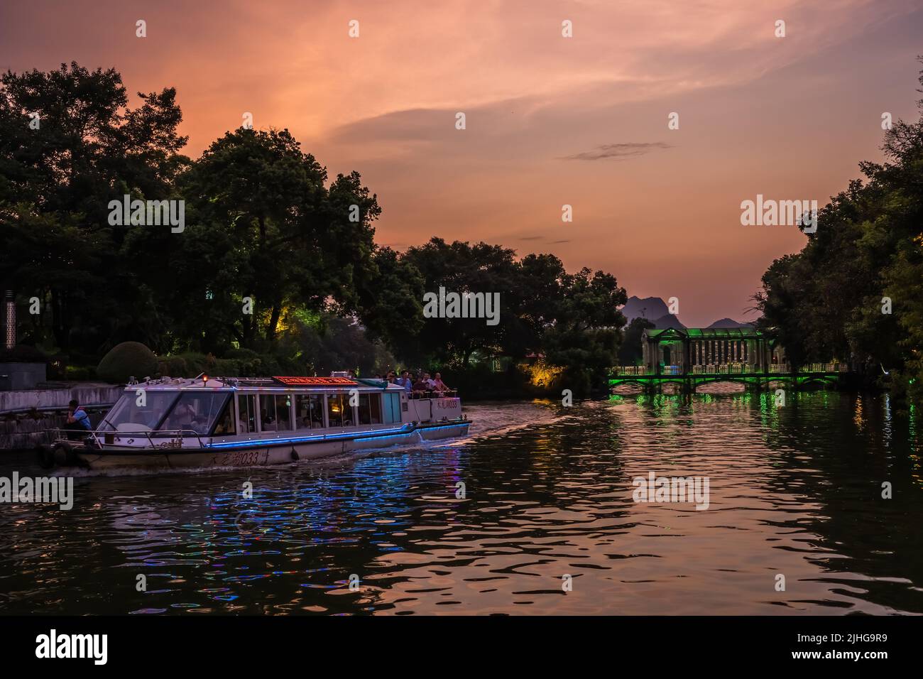Guilin, China - August 2019 : Sightseeing tour boat ferry carrying tourists sailing in front of Crystal glass bridge on the Shan Lake, Guilin town, Gu Stock Photo