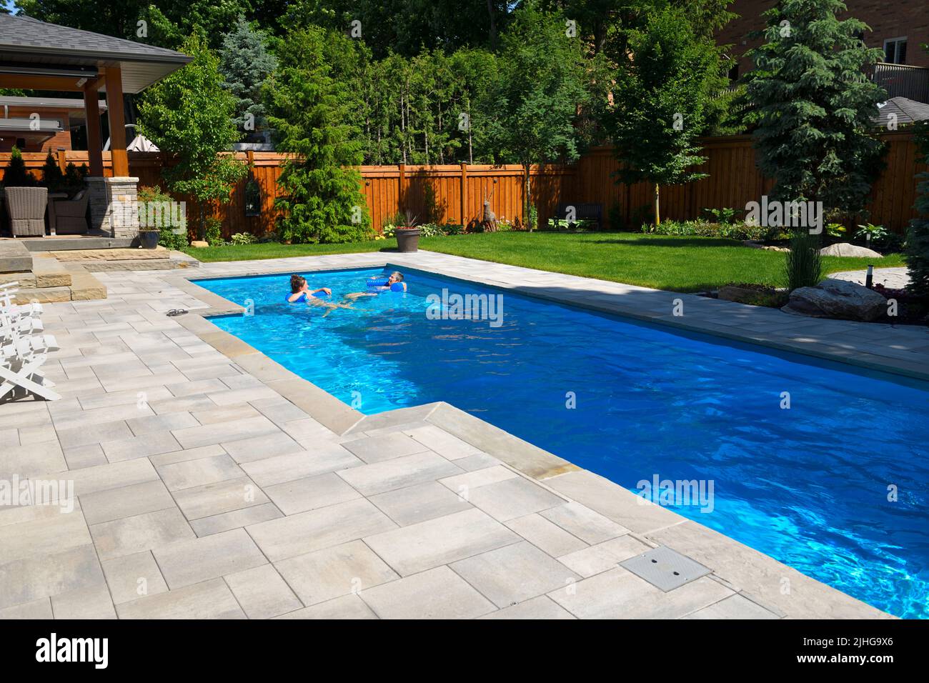 Mother and daughter swimming in new back yard pool with  patio of pavers and green lawn and gardens Stock Photo