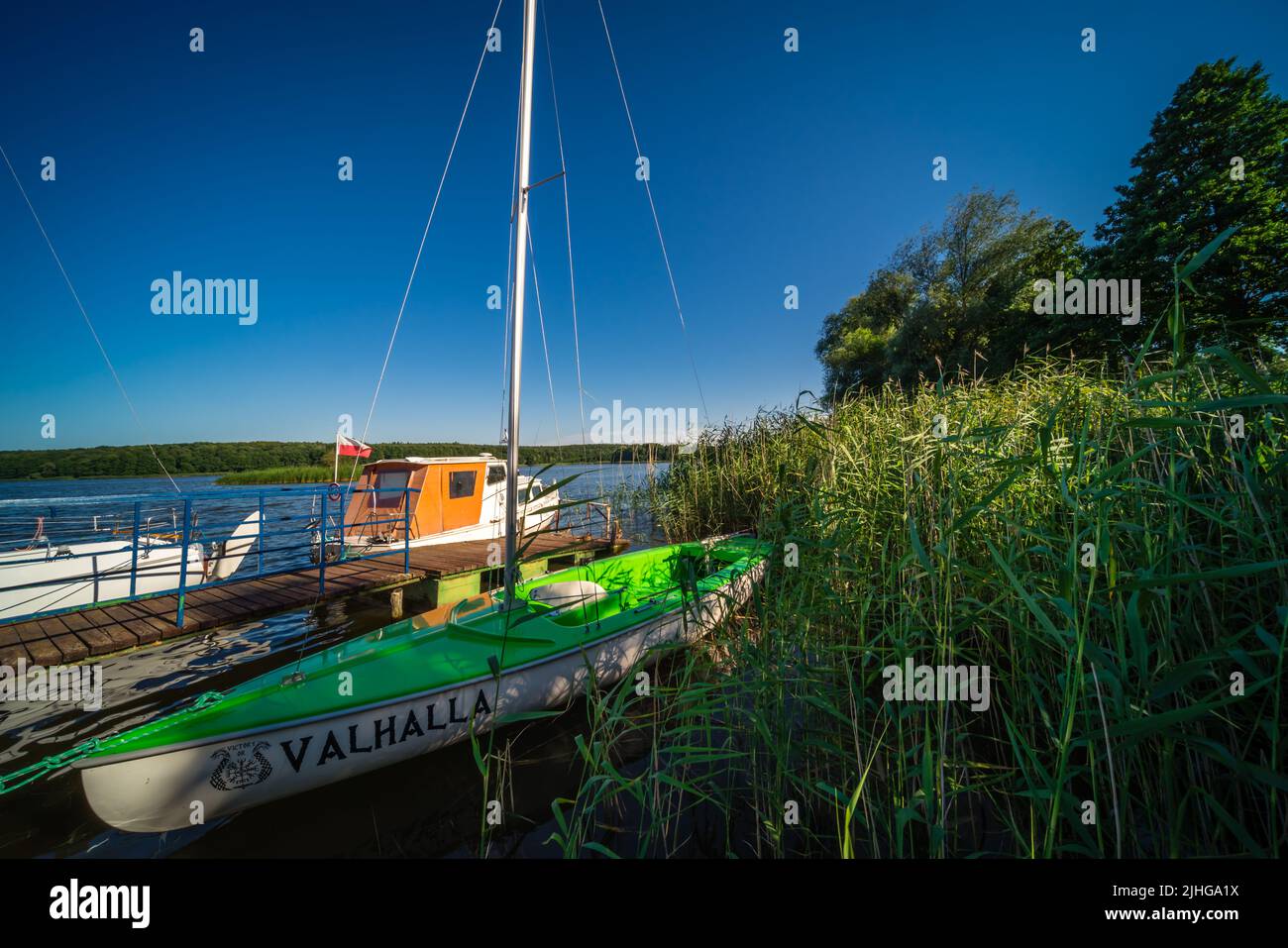 Jezioro Ostrowieckie, Poland - July 2020 : A small pier and private boats on the shore of a lake surrounded by reed and trees under the blue sky Stock Photo