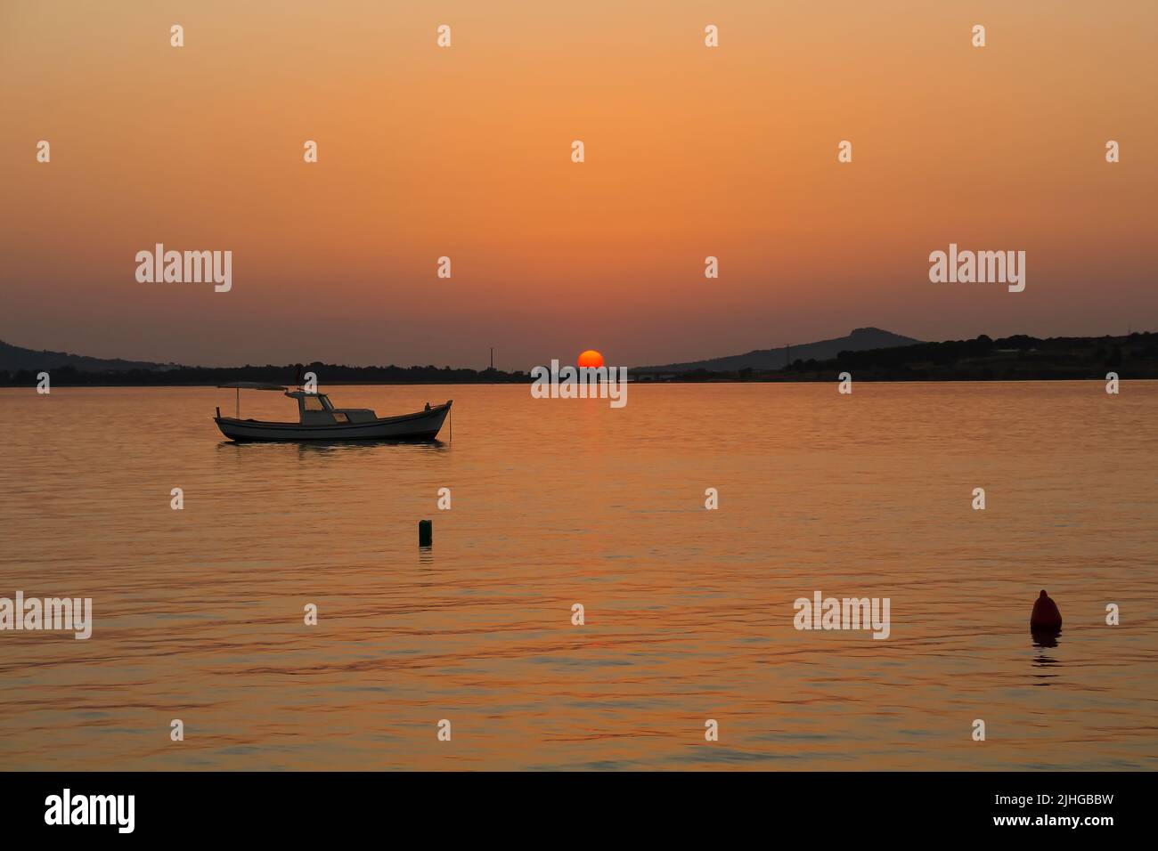 View of small, wooden fishing boat, Aegean sea and landscape at sunset captured in Ayvalik area of Turkey in summer. Beautiful scene. Stock Photo