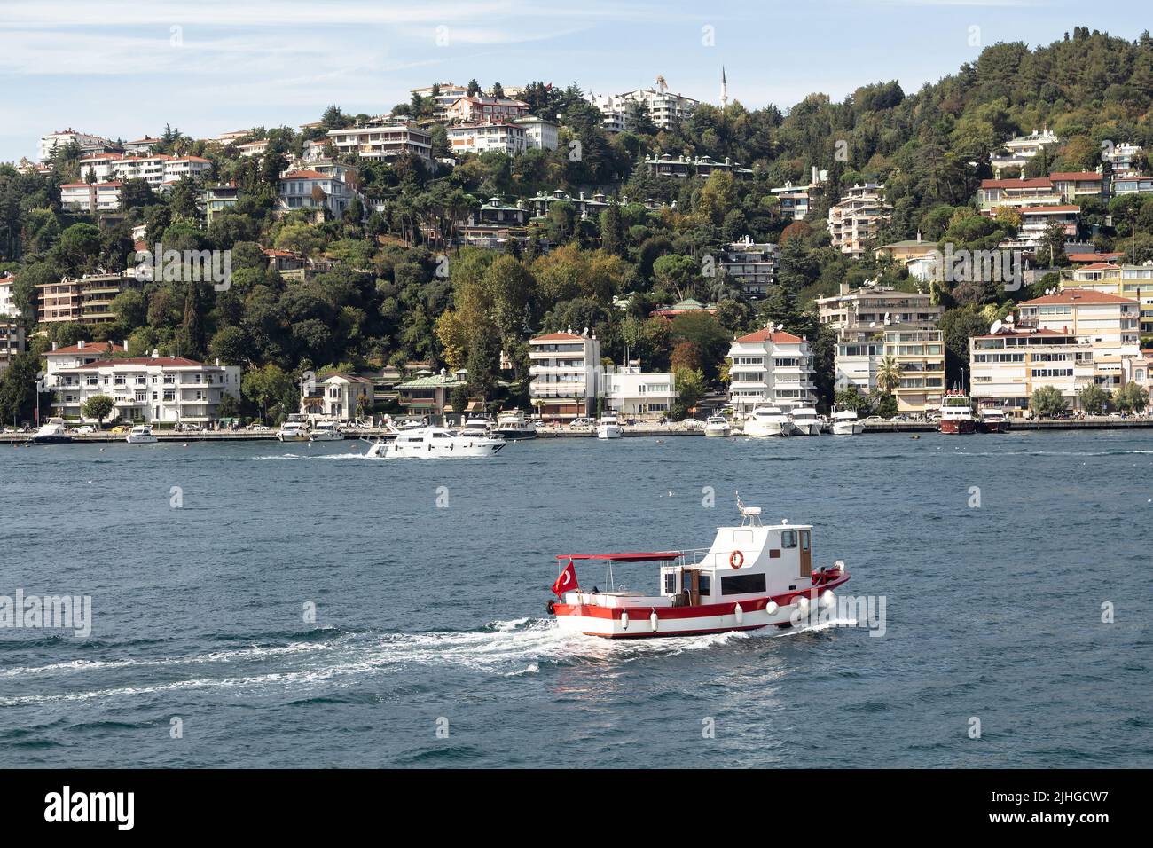 View of a fishing boat passing on Bosphorus and Bebek neighborhood on European side of Istanbul. It is a sunny summer day. Beautiful travel scene. Stock Photo