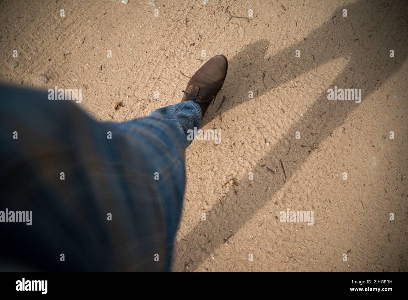 Close-up and overhead view of male businessman brown shoes walking on dirt road. Stock Photo