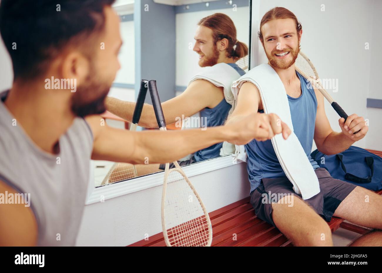 Two squash players giving each other a fist bump. Cheerful friends bonding in a gym locker room. Athletes being social and bonding with each other Stock Photo
