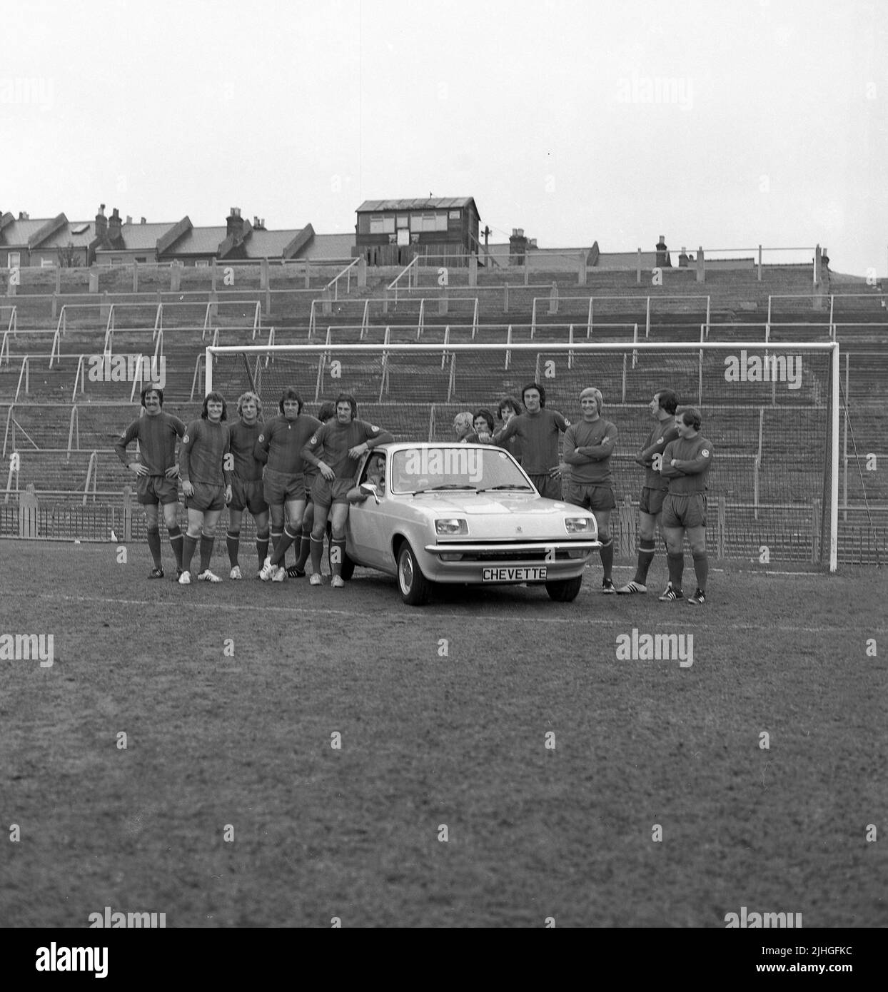 1974, historical, football manager, Malcolm Allison sitting in 2-door Chevette hatchback car on the pitch at Selhurst Park, with team players standing around. Selhurst Park is the home of Crystal Palace Football Club. A wooden hut on top of steep banked terraces says Police Post. Stock Photo