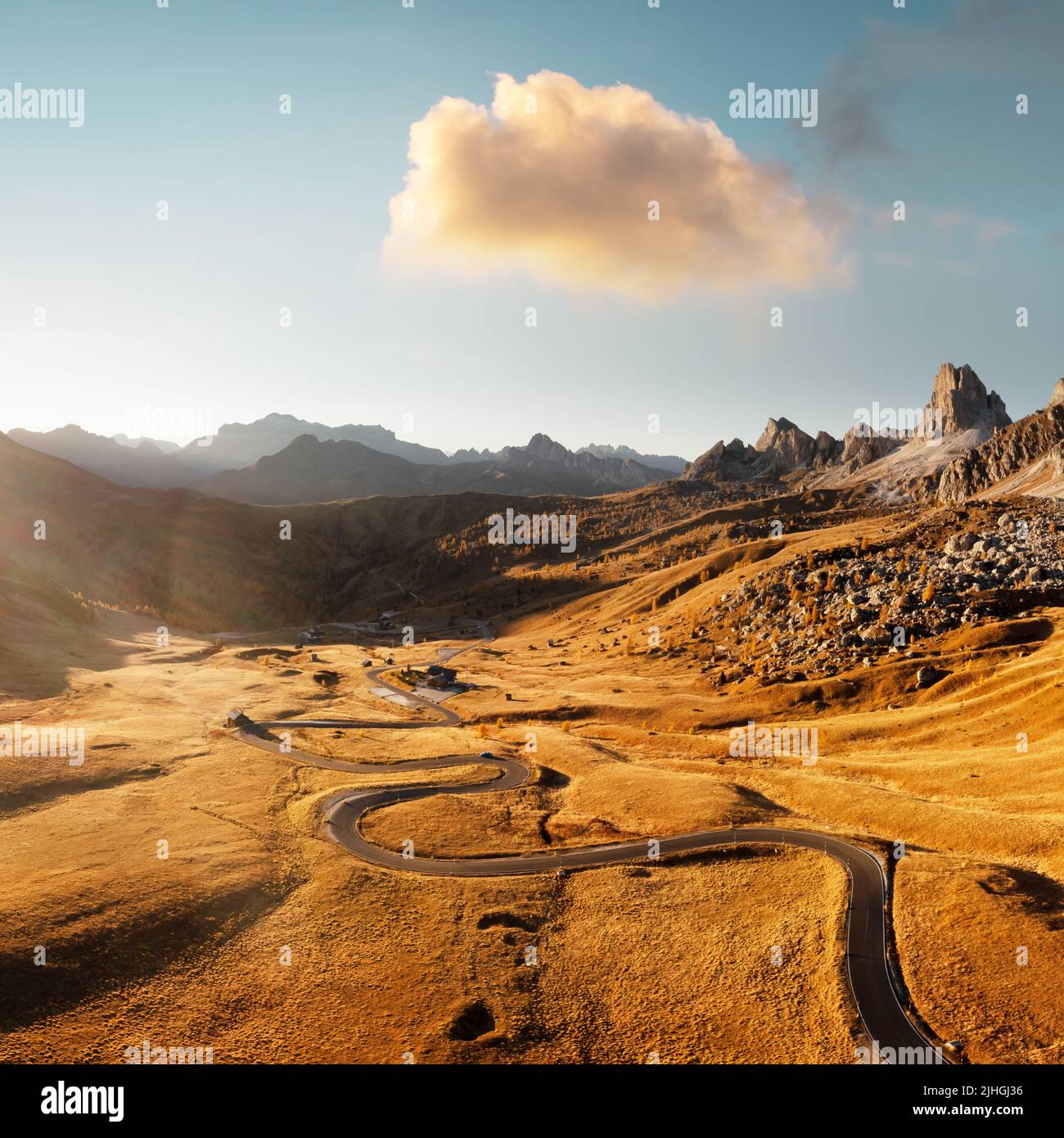 Picturesque aerial view on winding road in autumn mountain valley at sunset. The golden sunset light illuminates the mountains and orange grass. Passo Giau, Dolomite Alps, Dolomites, Italy Stock Photo