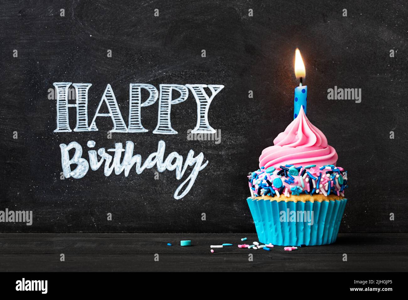 Birthday cupcake with birthday candle in front of chalkboard with happy birthday message Stock Photo