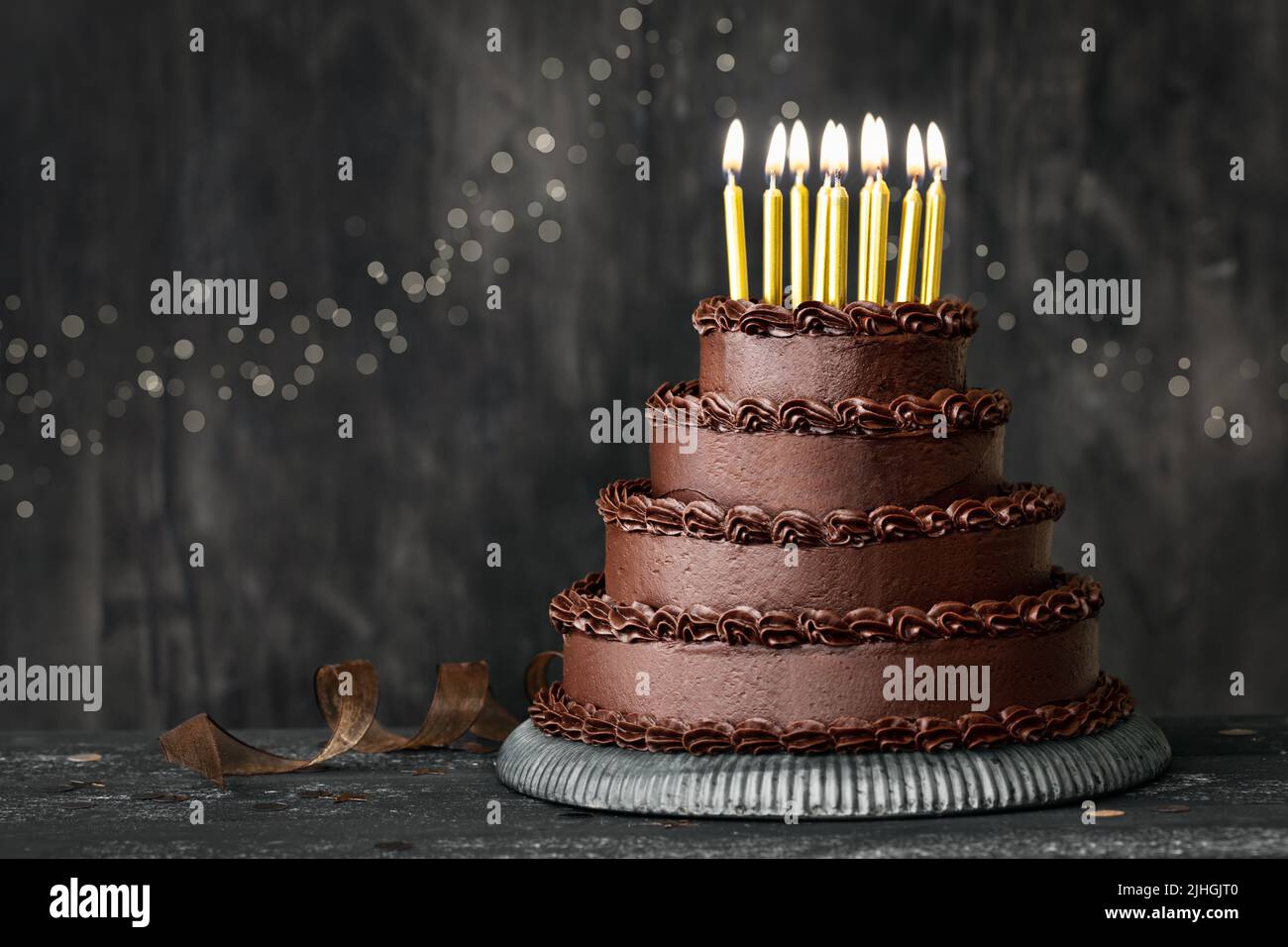 Tiered chocolate birthday cake decorated with chocolated frosting and gold birthday candles Stock Photo