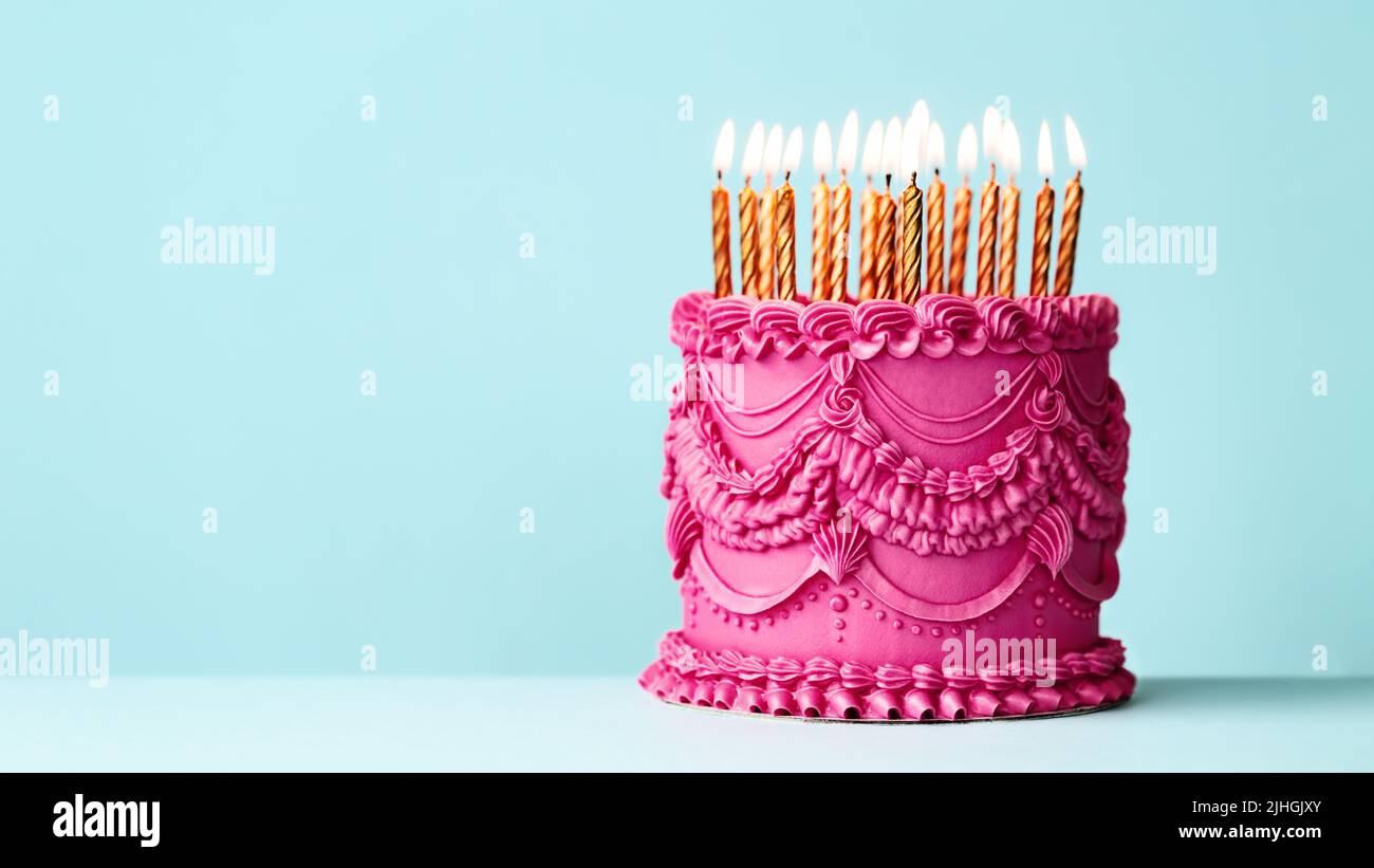 Fancy pink birthday cake with vintage style buttercream frills and ruffles and gold birthday candles against a blue background Stock Photo