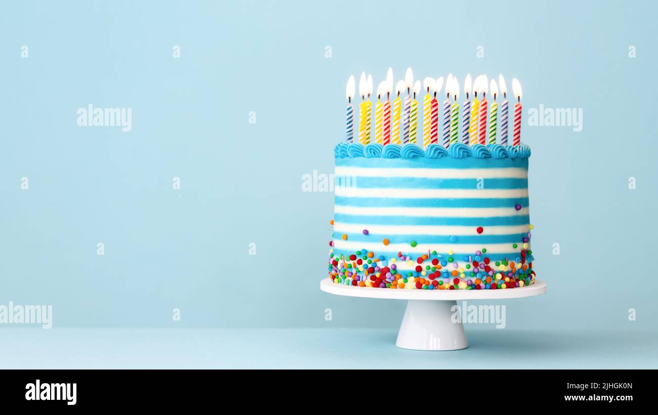 Striped buttercream birthday cake with colorful birthday candles and sprinkles on a blue background Stock Photo