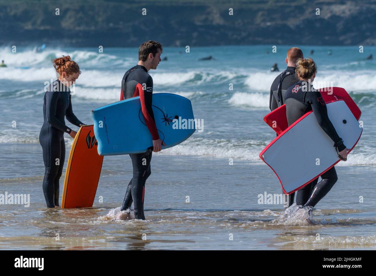 Holidaymakers carrying their bodyboards in the sea at Fistral in