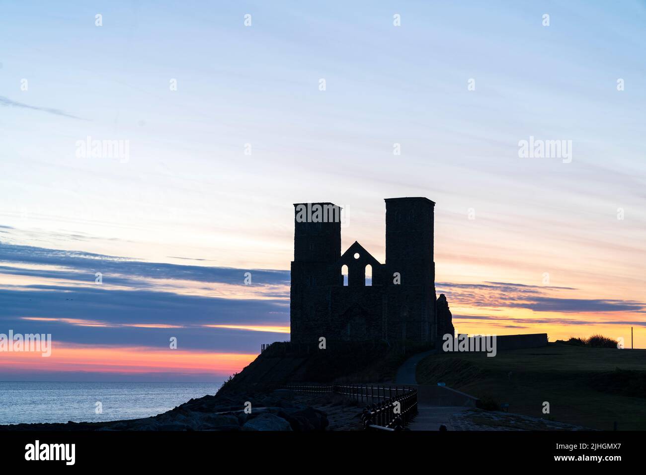 The dawn sky with the twin towers of the ruins of the 12th century church on the seafront at Reculver in Kent, England. Stock Photo
