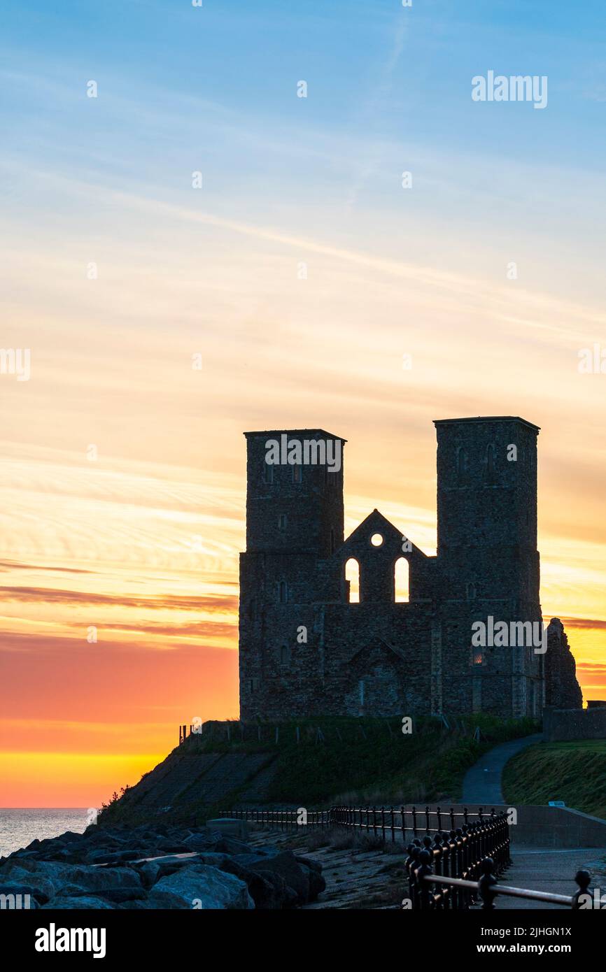 The dawn sky and sunrise behind the twin towers of the ruins of the 12th century church on the seafront at Reculver in Kent, England. Stock Photo