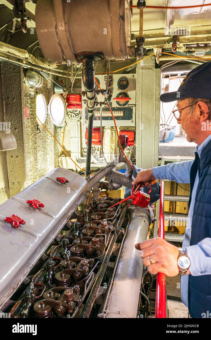 Man, engineer, oiling a large diesel engine in the engine room of the US navy P22 river patrol