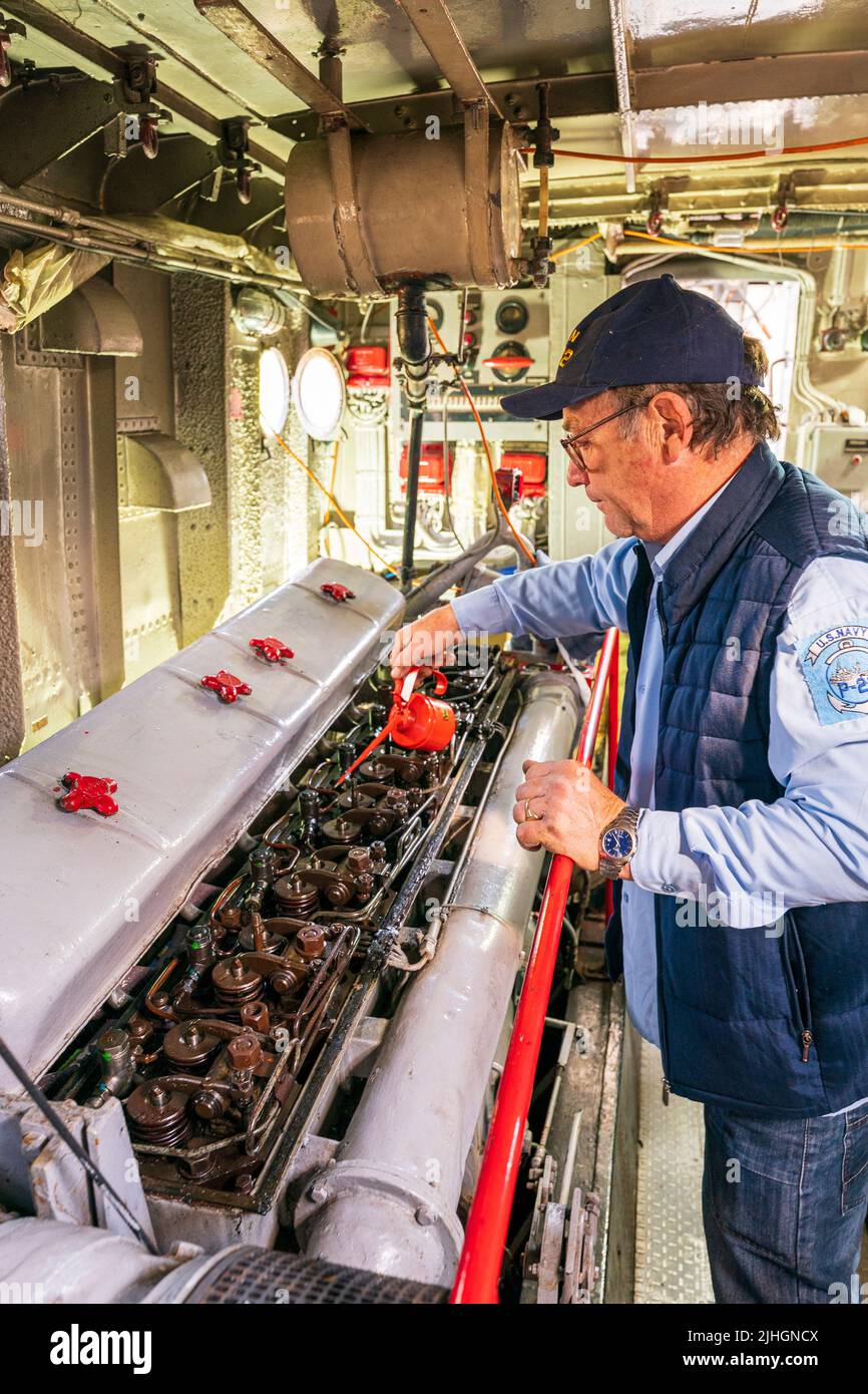 Man, engineer, oiling a large diesel engine in the engine room of the US navy P22 river patrol