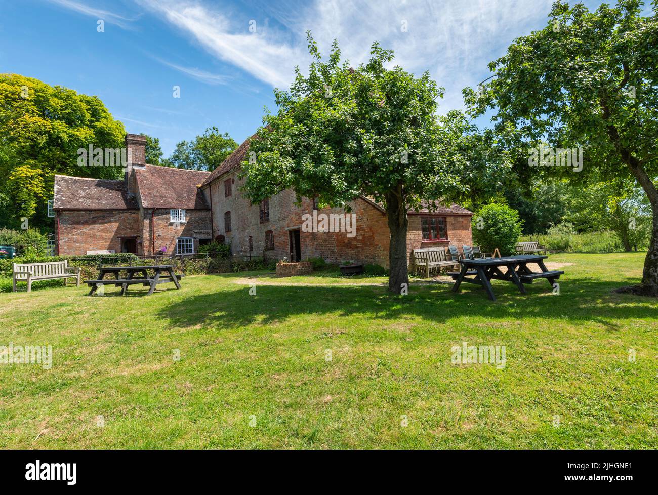 Back and garden of White Mill a 18th century corn mill powered by the river stour with apple trees and picnic tables with blue sky. Stock Photo