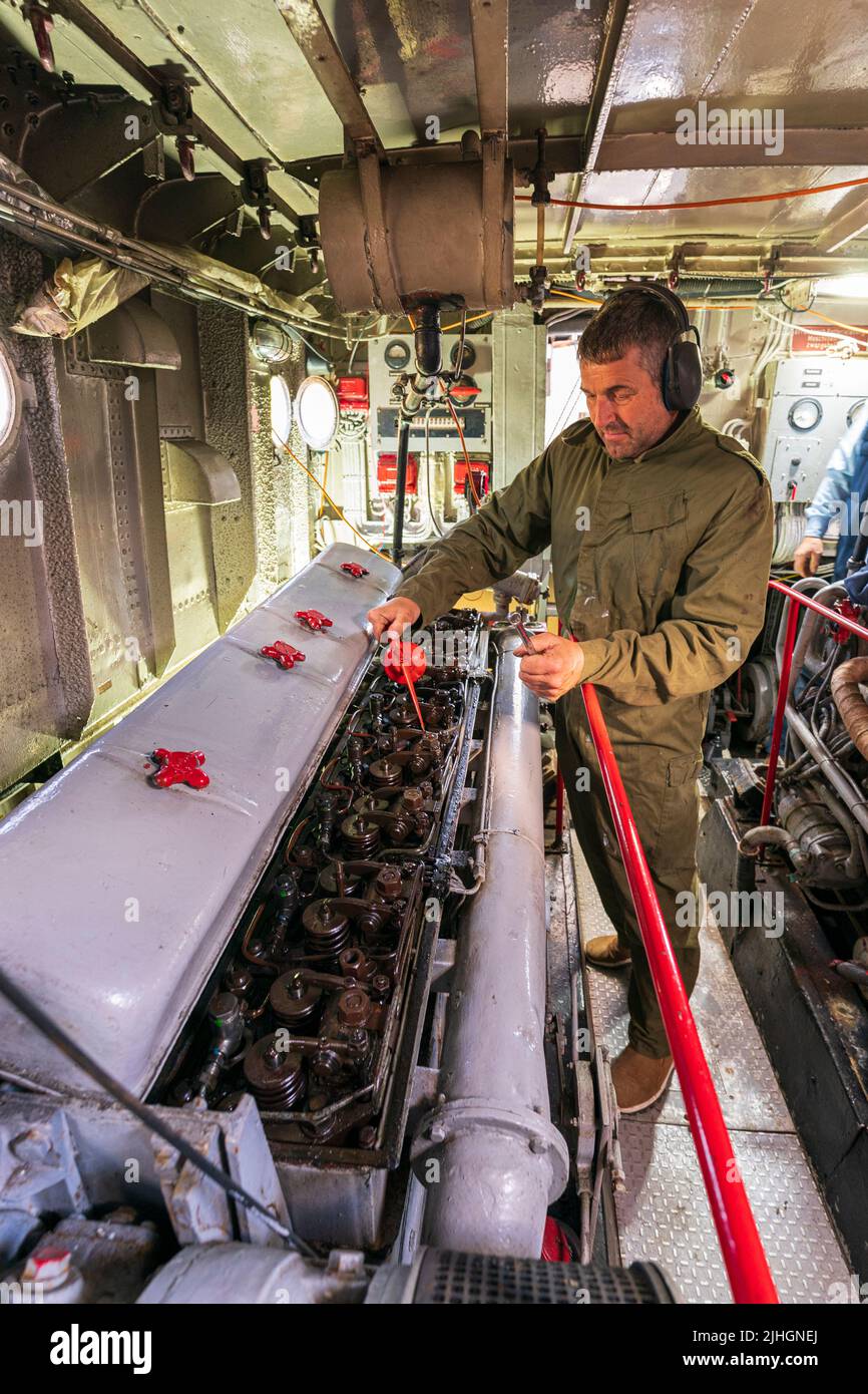 Man, engineer, oiling a large diesel engine in the engine room of the US navy P22 river patrol