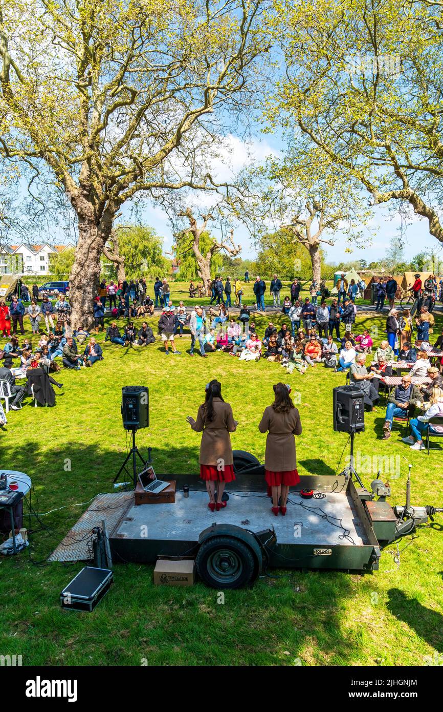 Two women singers on a small stage singing vintage songs to a mainly sitting audience on the green in bright sunshine at a 1940's event at Sandwich. Stock Photo