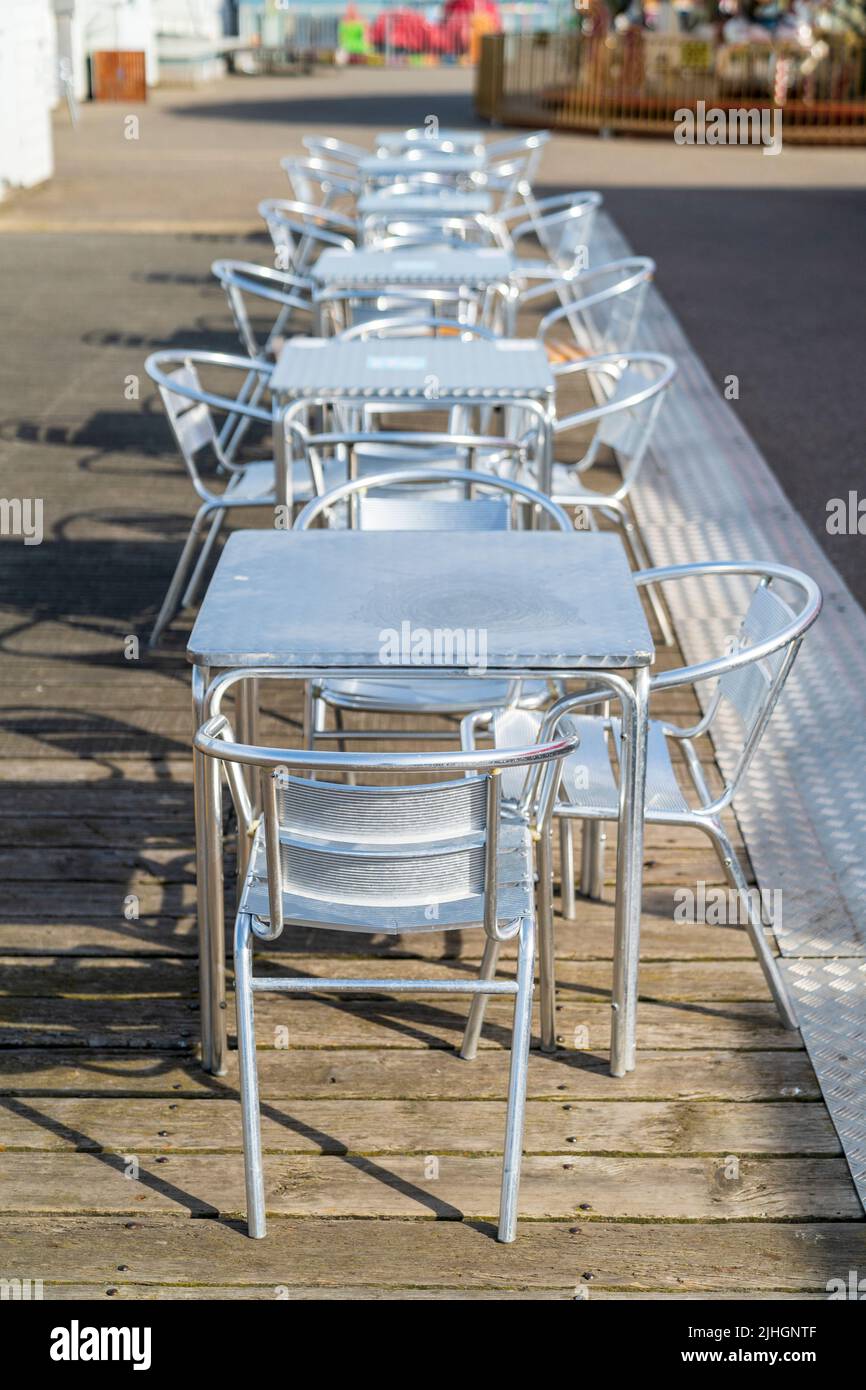 Row of six metal tables and chairs in a line on the empty pier at Herne Bay in the early morning. Selective narrow focus. Stock Photo