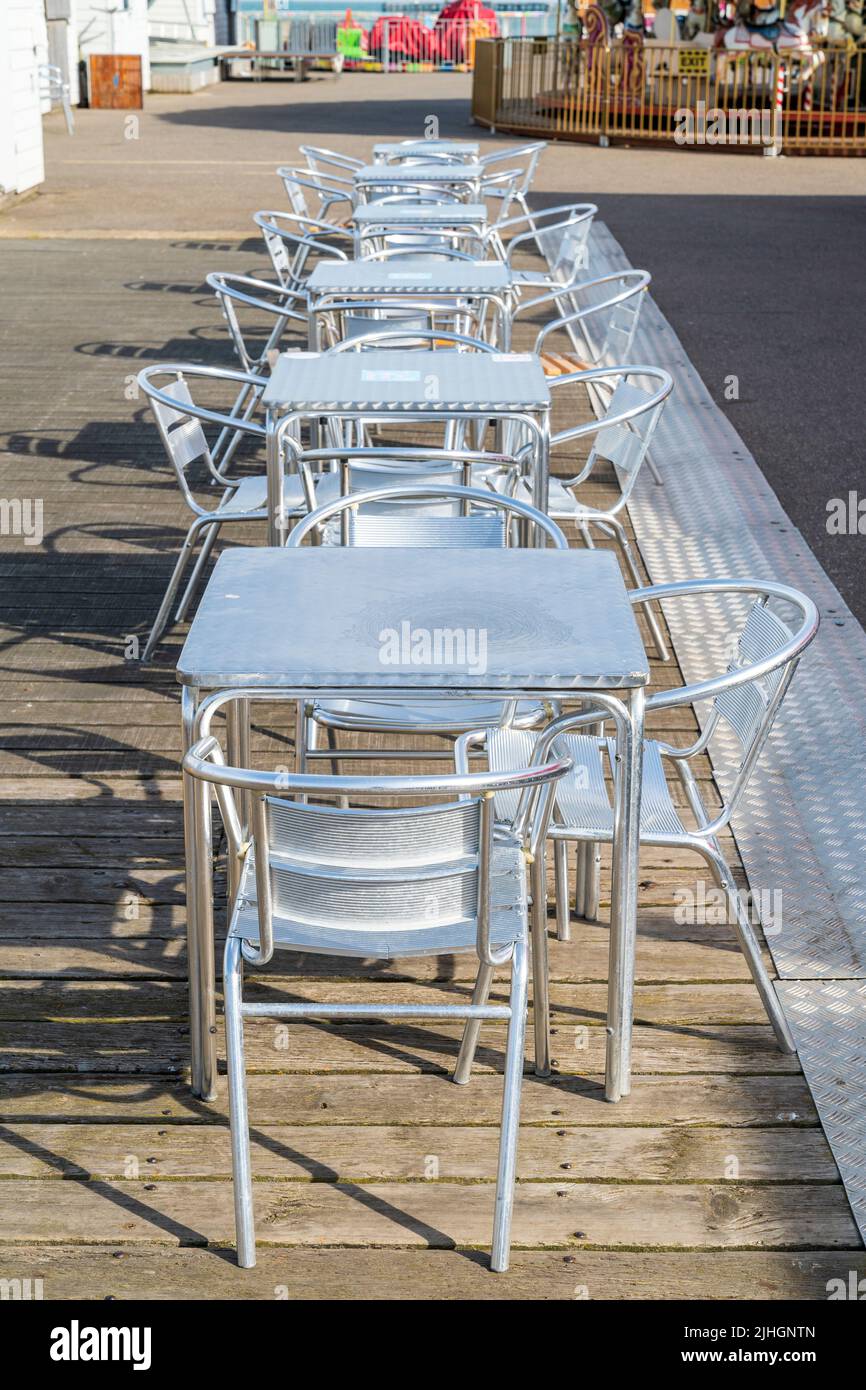 Row of six metal tables and chairs in a line on the empty pier at Herne Bay in the early morning. Stock Photo