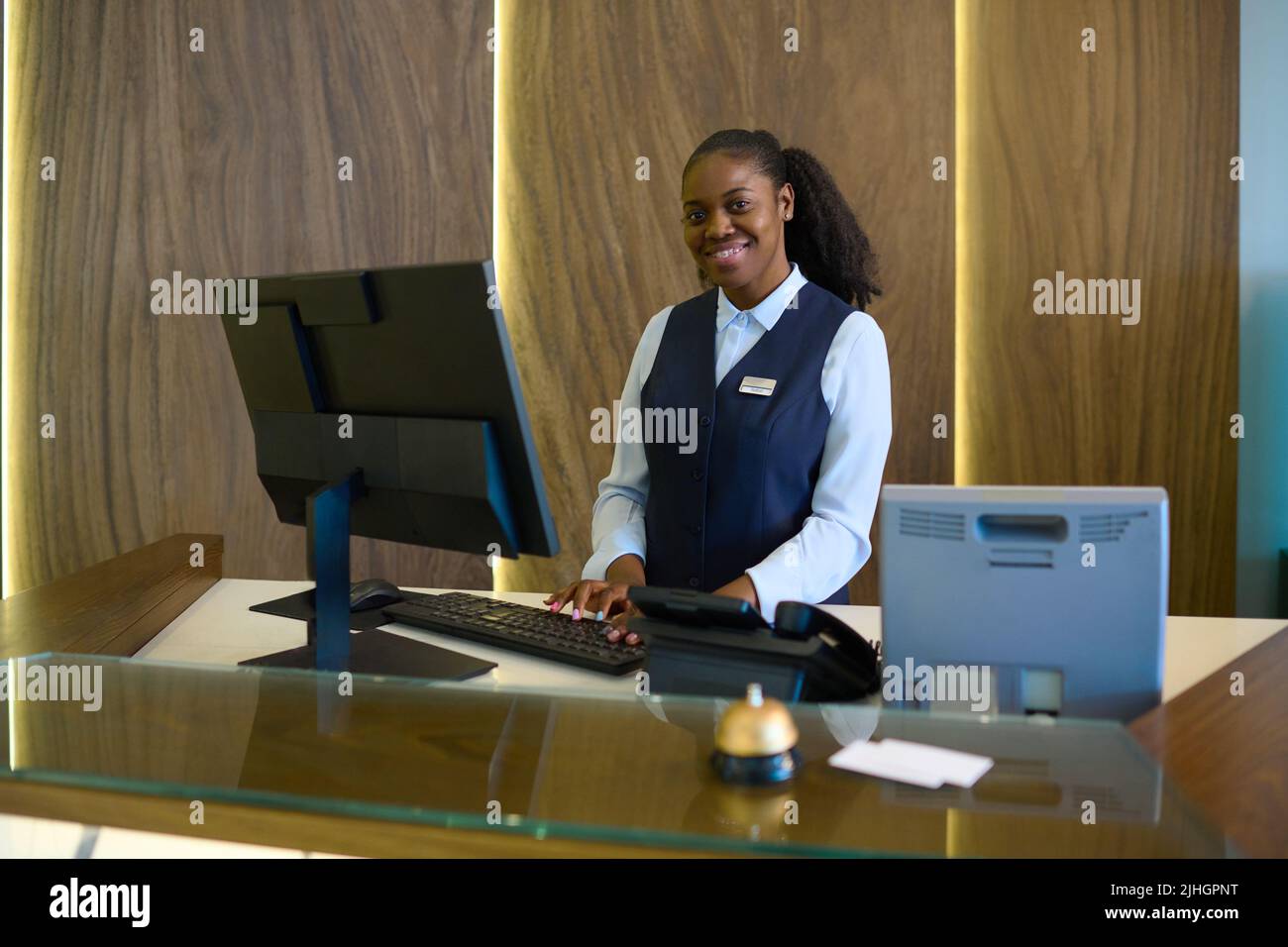 Happy young successful female receptionist in uniform standing by ...