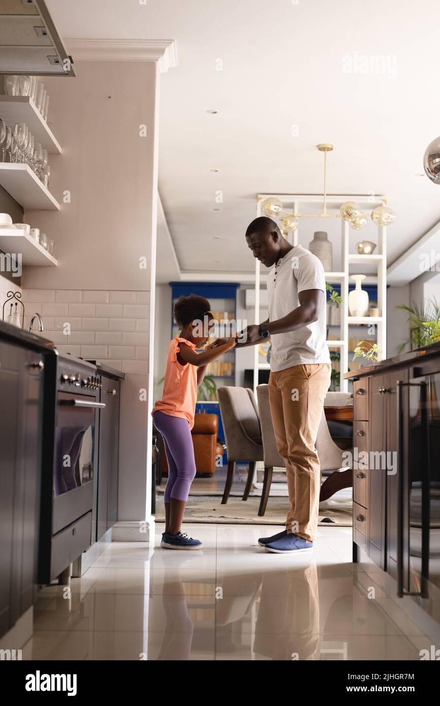 Vertical image of african american father and daughter dancing in kitchen Stock Photo