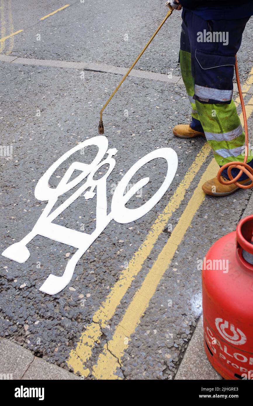 Image of a road worker burning on a white cycleway sign with a gas powered burner to indicate a