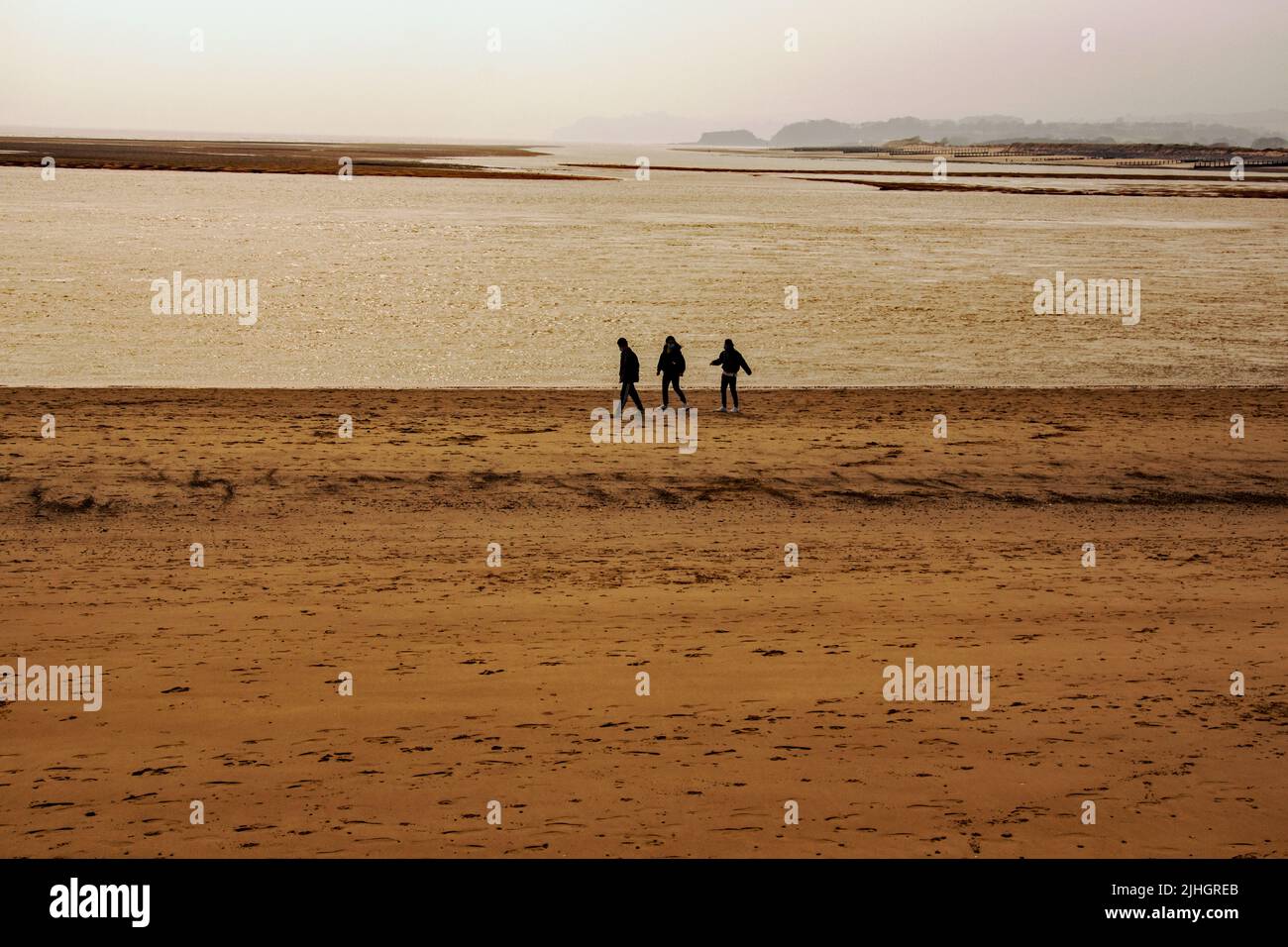 A group of three unknown walkers taking a walk on the beach in winter Stock Photo Alamy