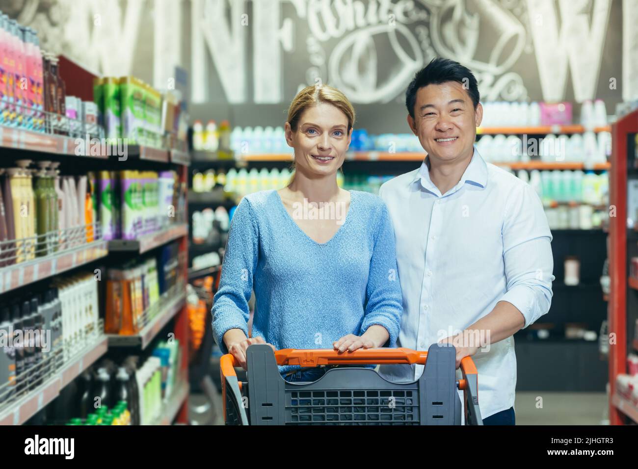 Portrait of happy shoppers in supermarket, interracial couple Asian man and woman, smiling and looking at camera, among shelves with goods Stock Photo