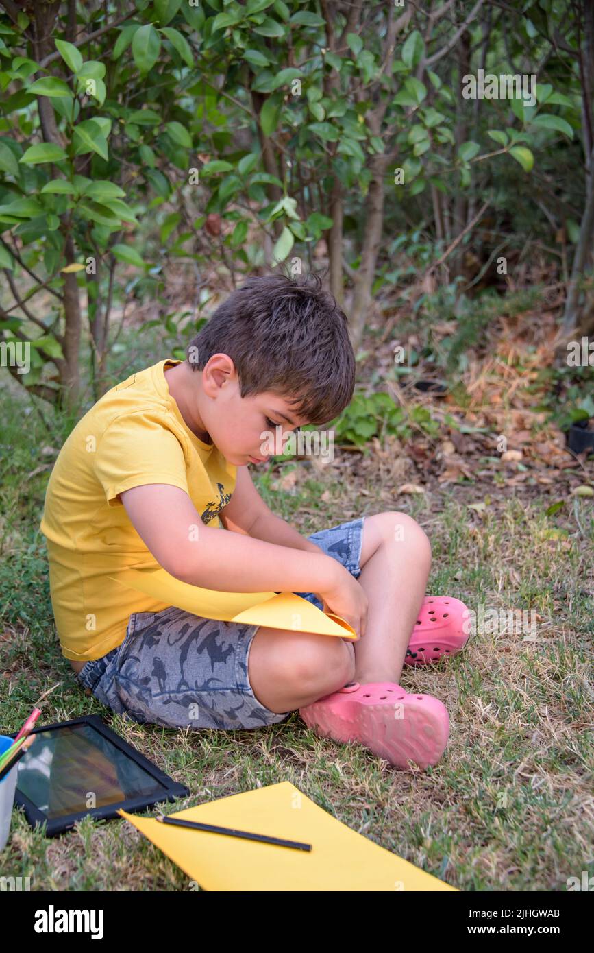 Kid draws in park laying in grass having fun on nature background. Stock Photo