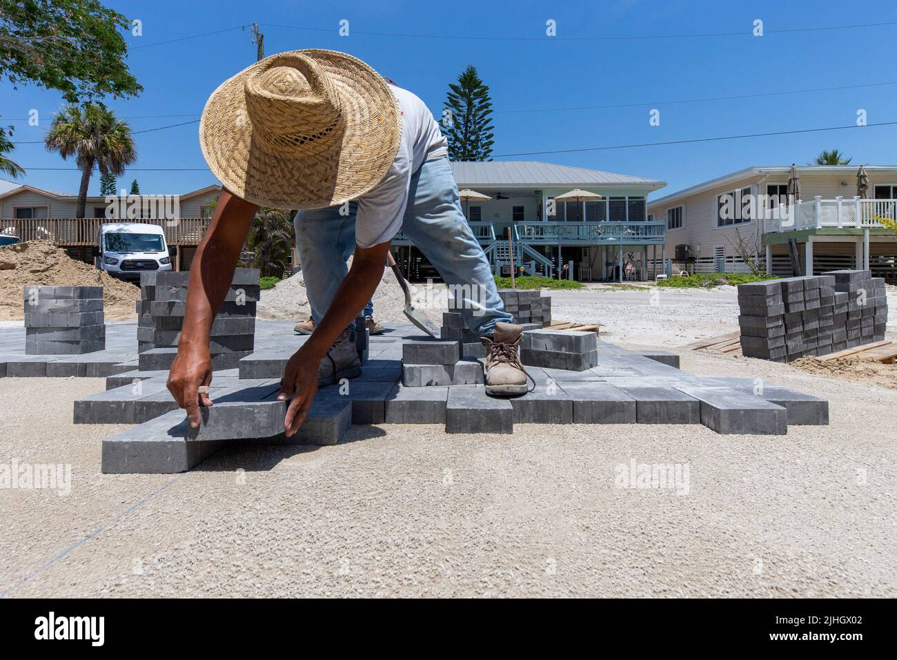 professional paver is laying down paving bricks on a prepared sandy surface to create a walk way and driveway to a new house under construction Stock Photo