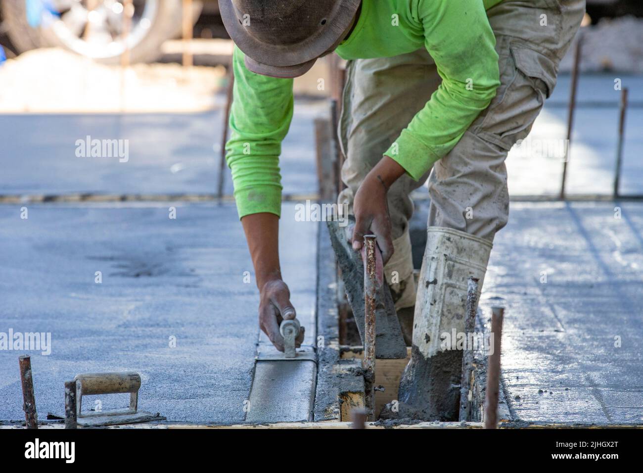 A construction worker is using a cornering trowel to finish the edge of a freshly poured concrete slap as a driveway. Stock Photo