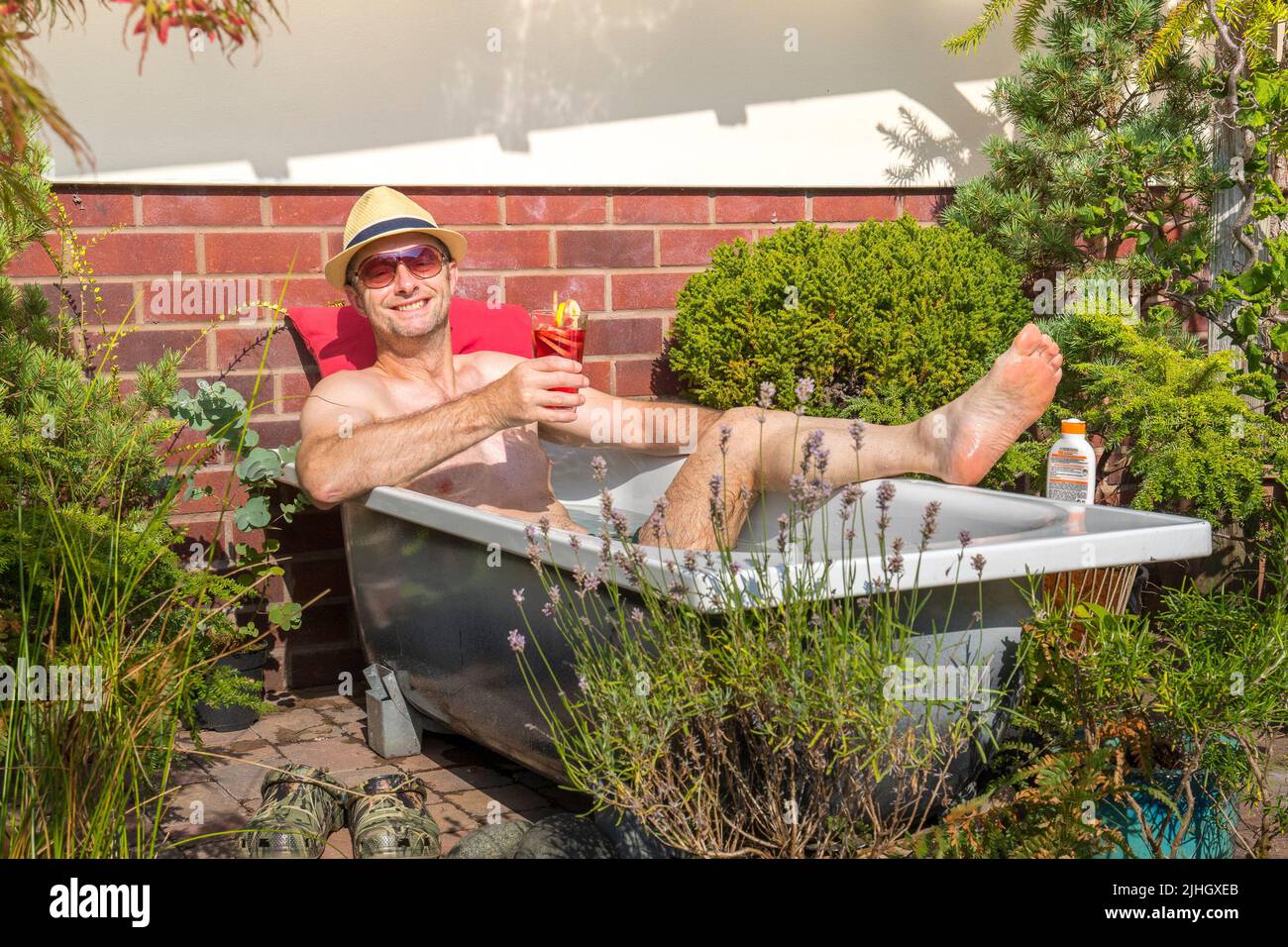Kidderminster, UK. 18th July, 2022. UK weather: with soaring temperatures there is only one way to cool down - Lee Hudson decides to take the day off and jump into his homemade plunge pool! Today's scorching heat gives perfect opportunity to reuse an old bath tub as a plunge pool for the day before recycling the old tub. Cold water in the tub reached 28 degrees by mid-afternoon making it ideal for a soothing dip and a fruity drink to rehydrate. Credit: Lee Hudson/Alamy Live News Stock Photo